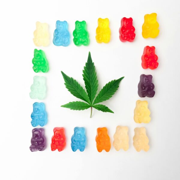Vibrant gummy bears form a colorful border around a cannabis leaf on a white background, showcasing edible cannabis culture.
